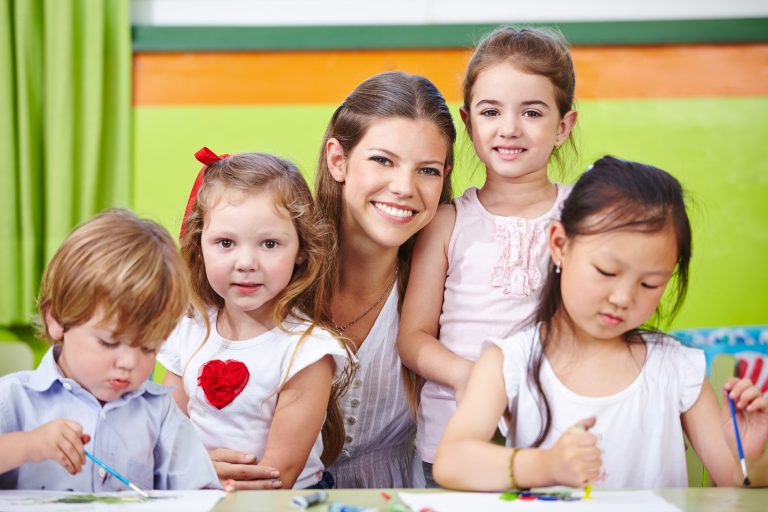 Lächelnder Erzieher und glückliche Kinder im Kindergarten malen